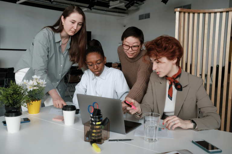 Four people collaborating and looking down at a laptop together